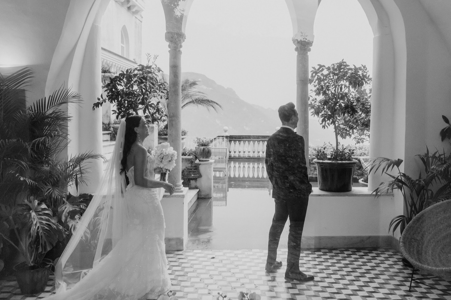 A black and white photo of a bride and groom in the arched, plant-filled loggia of Palazzo Avino in Ravello