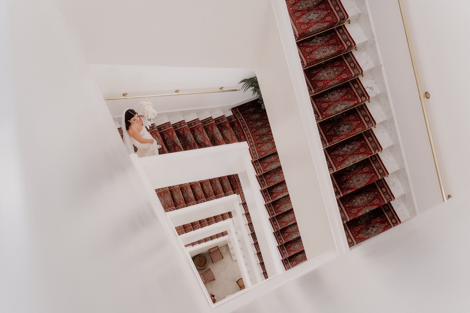 The red-carpeted staircase of Palazzo Avino in Ravello, seen from above with the bride on the stairs