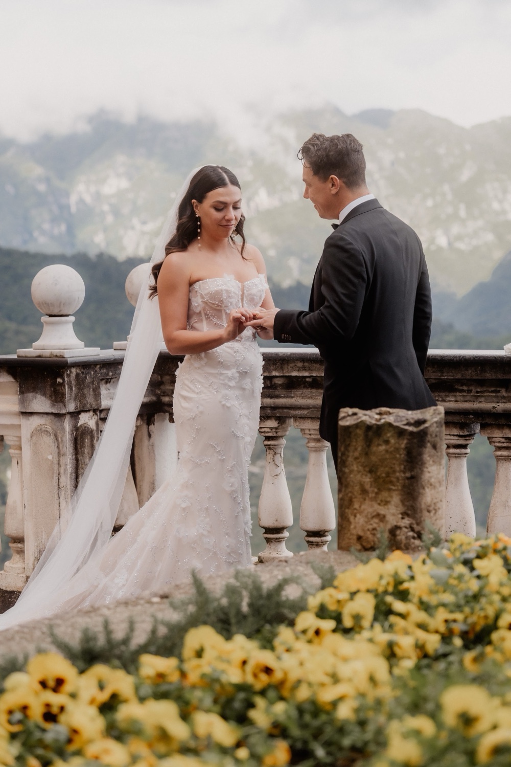 A couple on a stone balcony above the Amalfi Coast at Palazzo Avino in Ravello, with yellow flowers in front of them