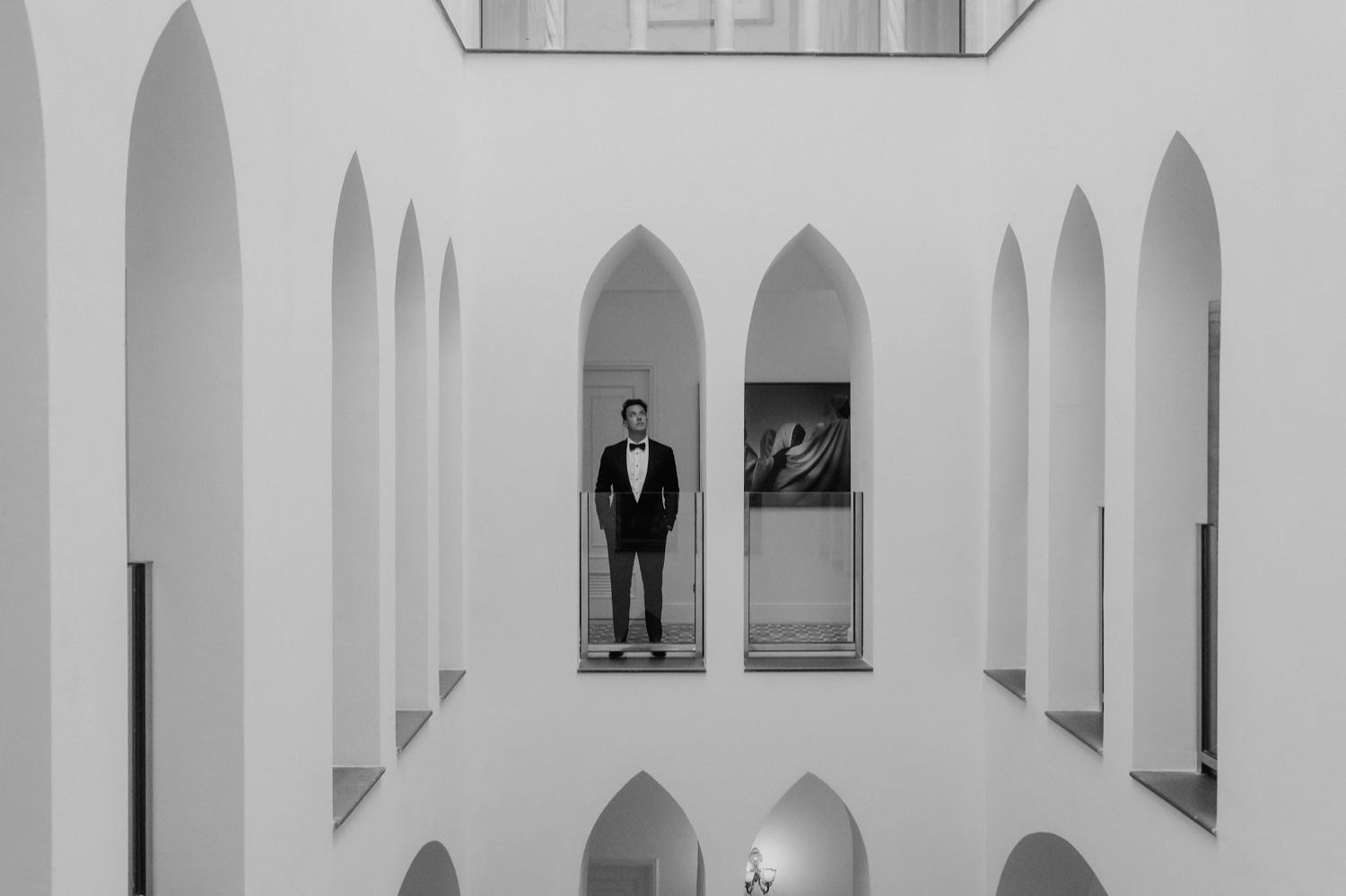 A black and white photo of a groom standing in a pointed arch of the white courtyard at Palazzo Avino in Ravello