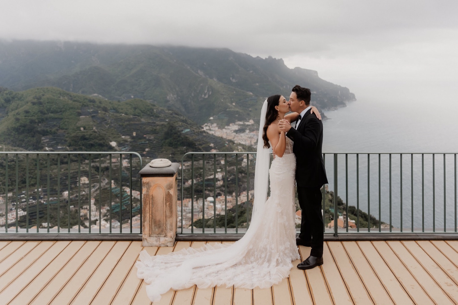 A couple kissing on a terrace at Palazzo Avino in Ravello, with the green hills and the sea of the Amalfi Coast below