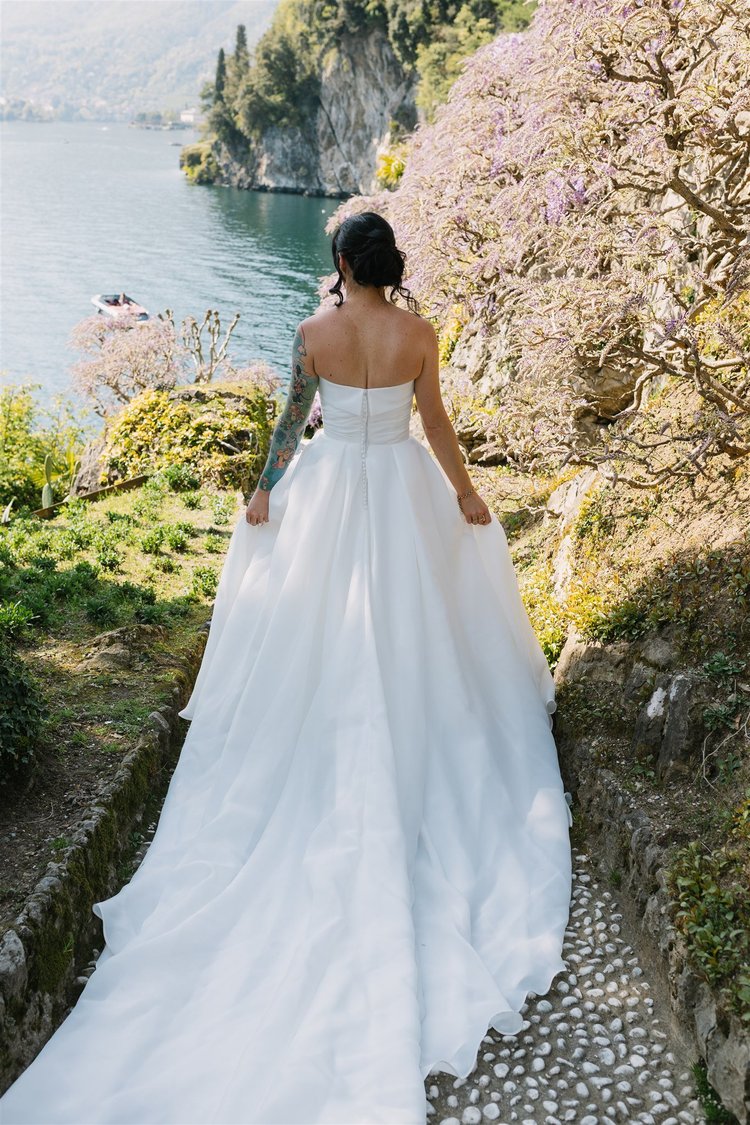 A bride walking down a garden path lined with wisteria
