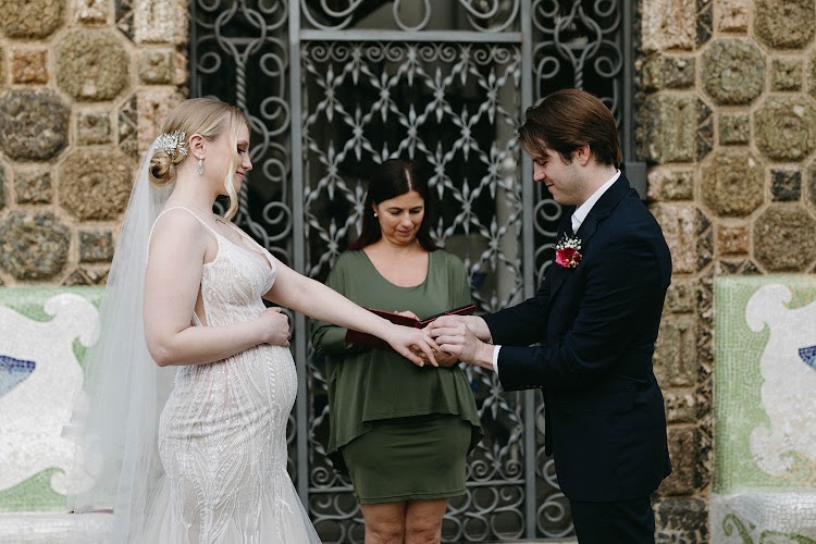 A couple exchanging rings during their elopement ceremony in front of the wrought-iron door and mosaic stone wall of Bellesguard Tower, a Gaudí building in Barcelona