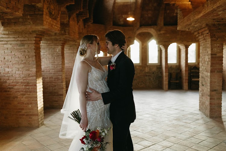 A couple embracing inside the brick attic of Bellesguard Tower, a Gaudí building in Barcelona, with its Gothic arched windows and vaulted ceiling
