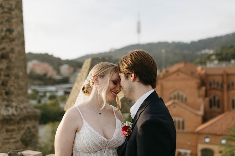 A couple touching foreheads on the terrace of Bellesguard Tower, a Gaudí building in Barcelona, with the stone spire and Barcelona rooftops behind