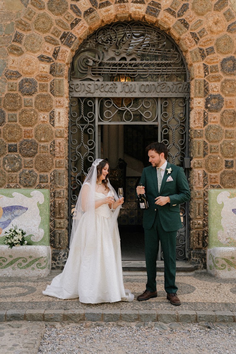 A newlywed couple toasting at the Gaudí stone entrance door of Bellesguard Tower in Barcelona