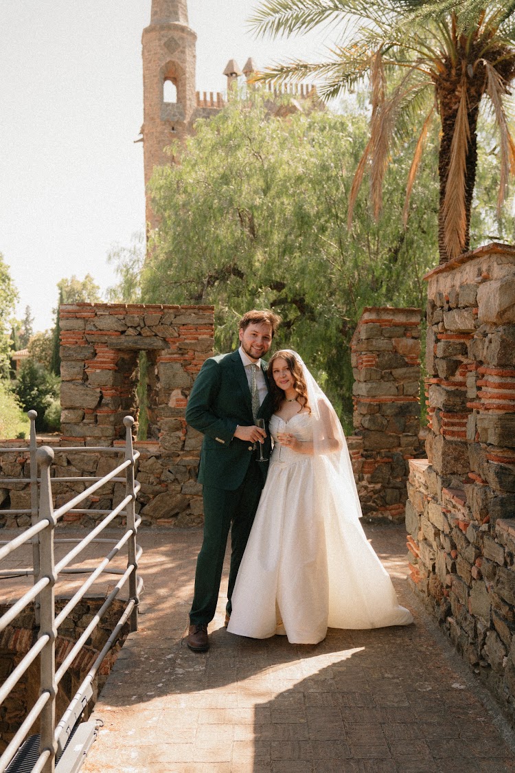 A couple posing in the gardens of Bellesguard Tower, a Gaudí building in Barcelona, with the spire above the trees
