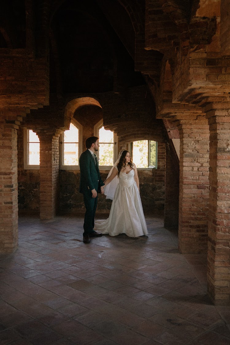 A bride and groom in the brick attic of Bellesguard Tower in Barcelona with light streaming through arched windows
