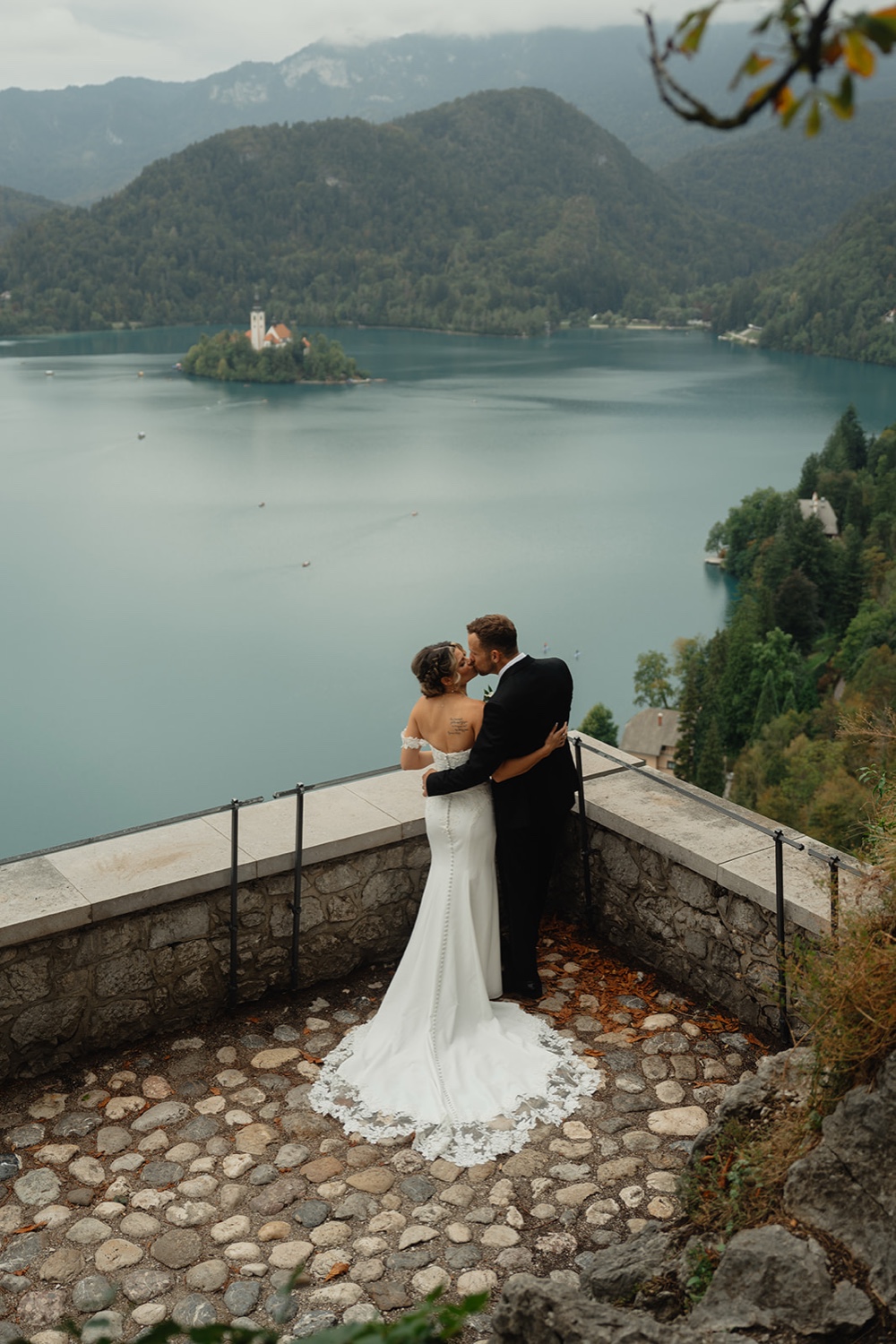 A couple kissing on the stone terrace of Bled Castle, with Lake Bled and its island below, Slovenia