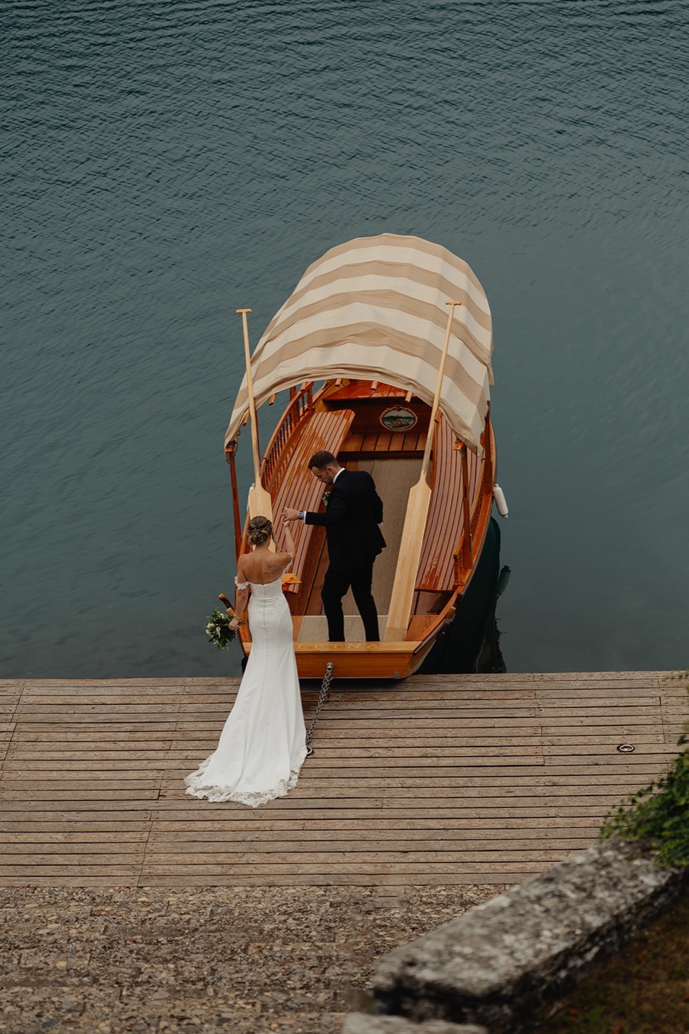 A bride and groom stepping onto a traditional Pletna boat at the shore of Lake Bled, Slovenia