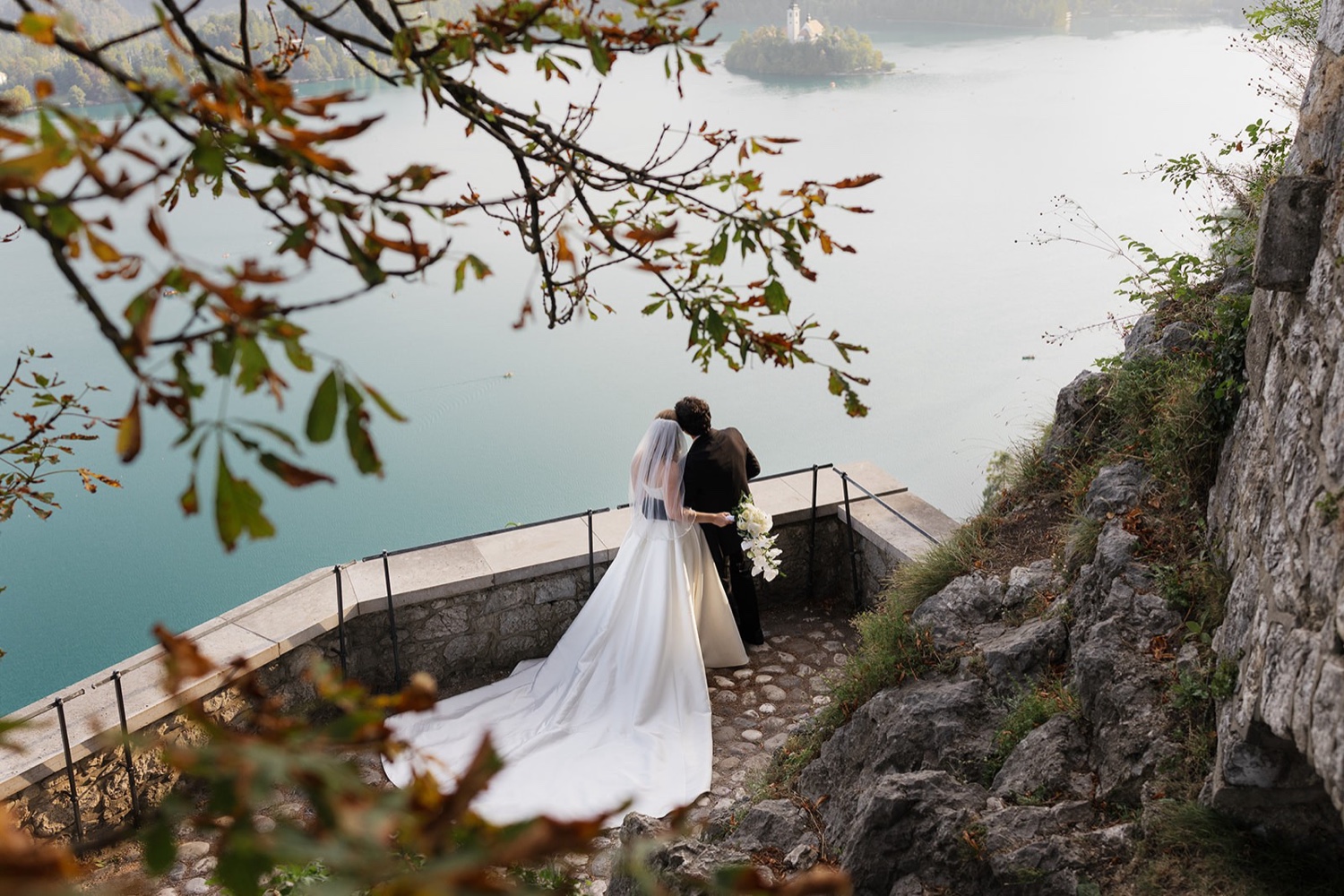 A couple looking out over Lake Bled from a terrace at Bled Castle, framed by autumn leaves, Slovenia