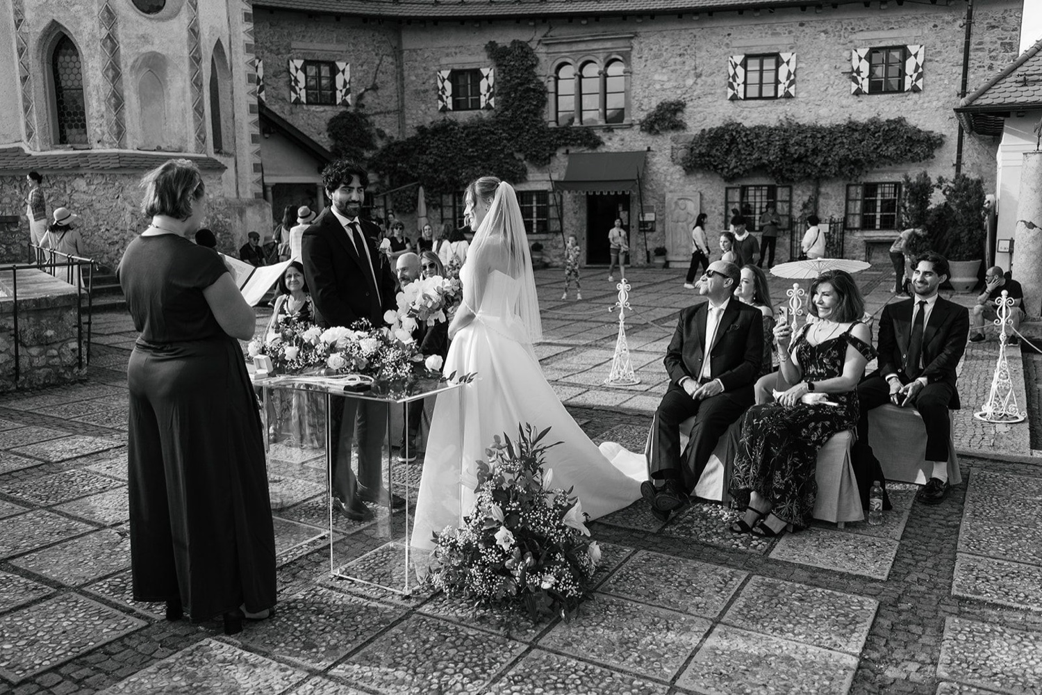 A black and white photo of a ceremony in the courtyard of Bled Castle, with guests watching, Slovenia