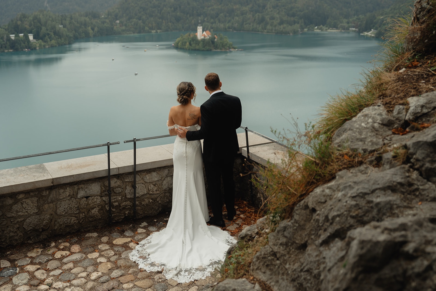 A couple standing on the stone terrace of Bled Castle, looking out over Lake Bled and its island