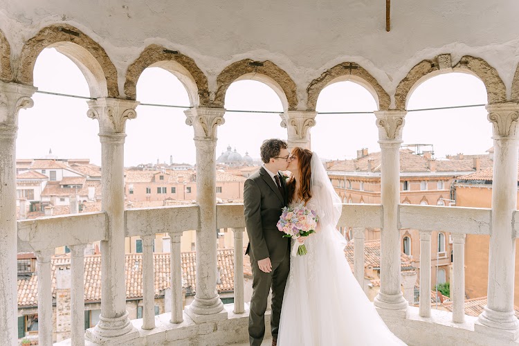 A kiss under the arches of the belvedere, above the rooftops of Venice