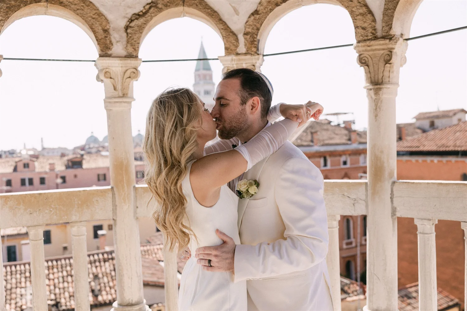 A couple kissing on the belvedere at the top of the Scala Contarini del Bovolo, above the rooftops of Venice
