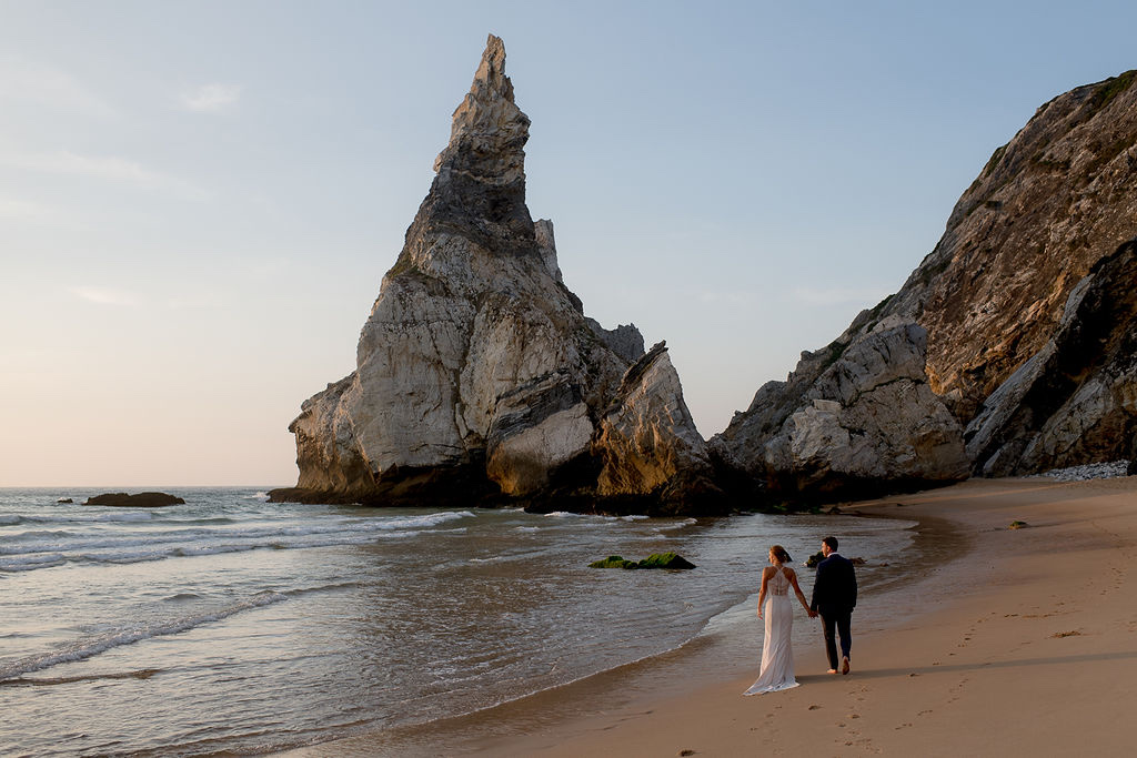 A couple walking on the beach beside a sea stack near Cabo da Roca in Sintra, Portugal