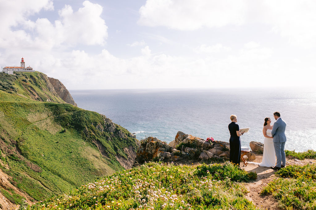 A couple exchanging vows on a clifftop at Cabo da Roca in Sintra, Portugal, with the lighthouse and the Atlantic behind them