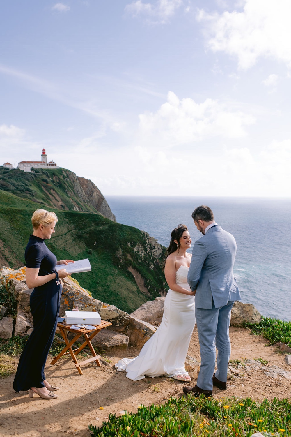 A couple exchanging vows with their celebrant on the cliffs of Cabo da Roca in Sintra, Portugal, with the lighthouse behind