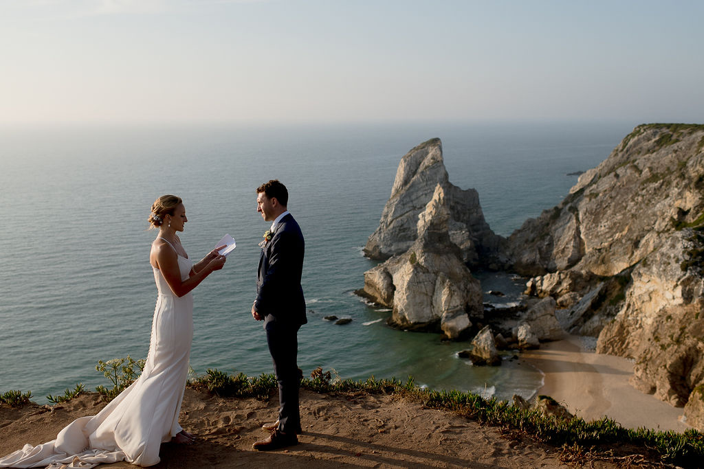 A couple reading their vows on the cliff edge at Cabo da Roca in Sintra, Portugal, with sea stacks behind