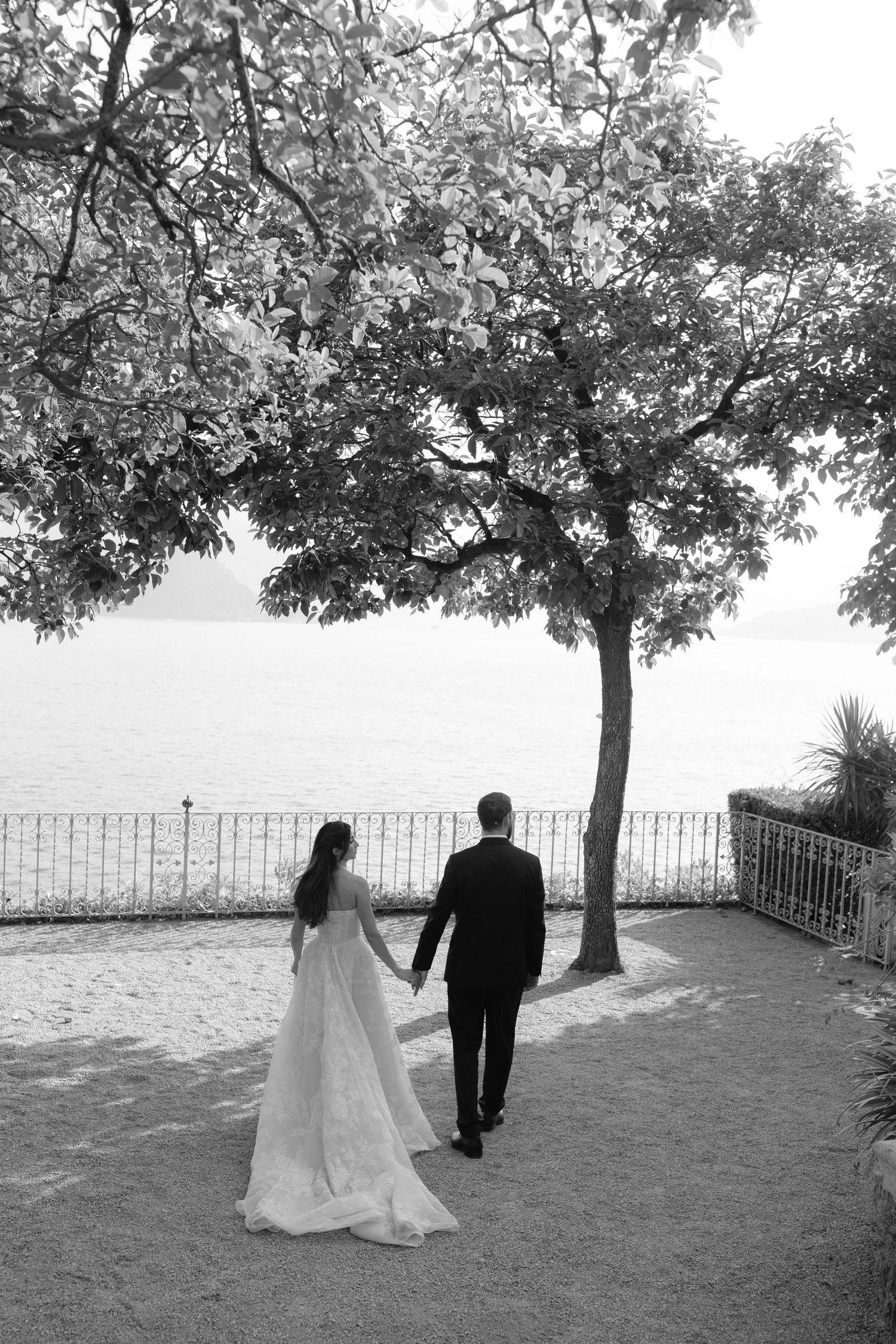 A couple walking towards the lake under the trees at Villa Cipressi