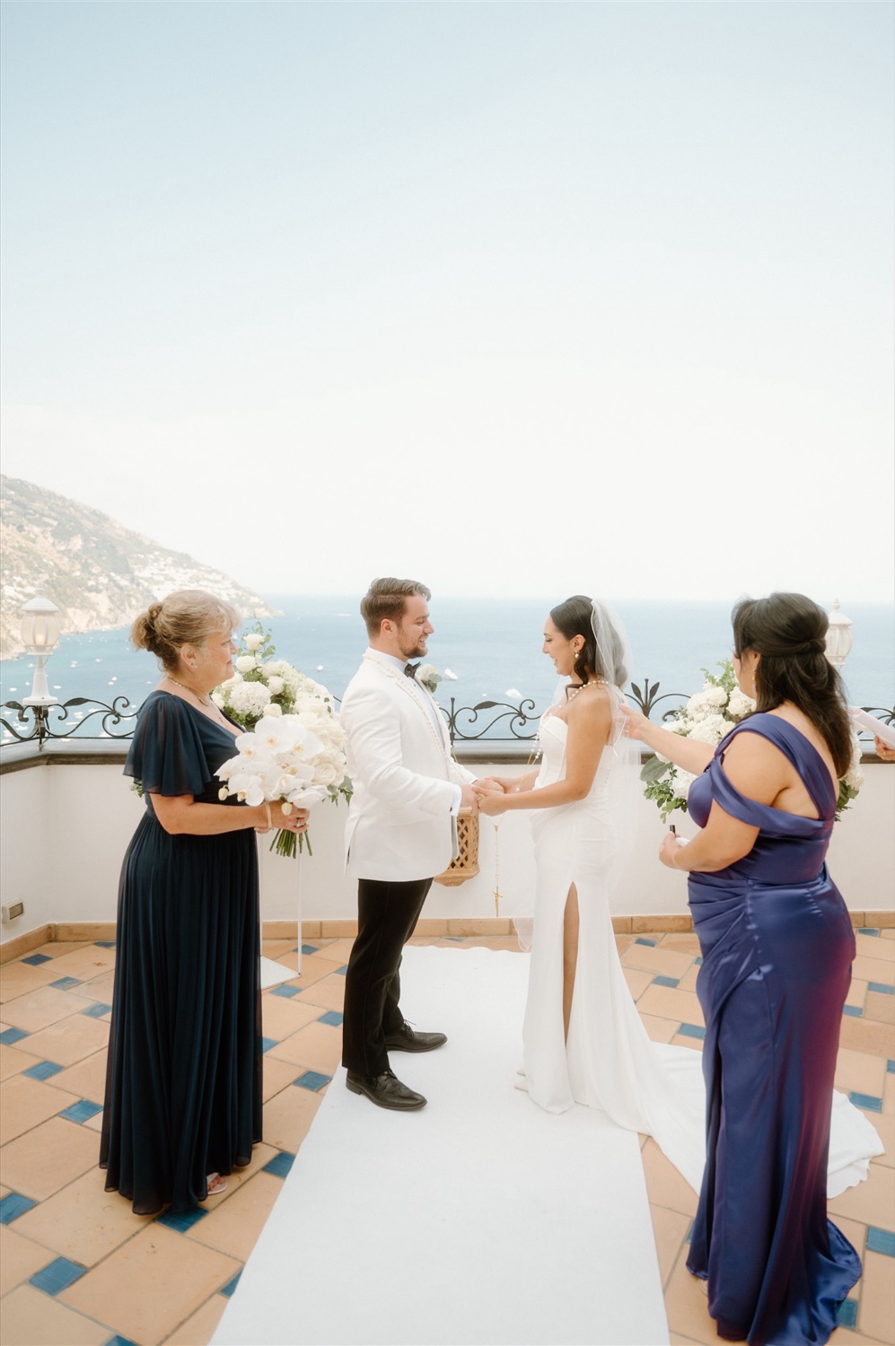 A bride and groom holding hands with their guests beside them on the rooftop terrace of Hotel Conca d’Oro in Positano