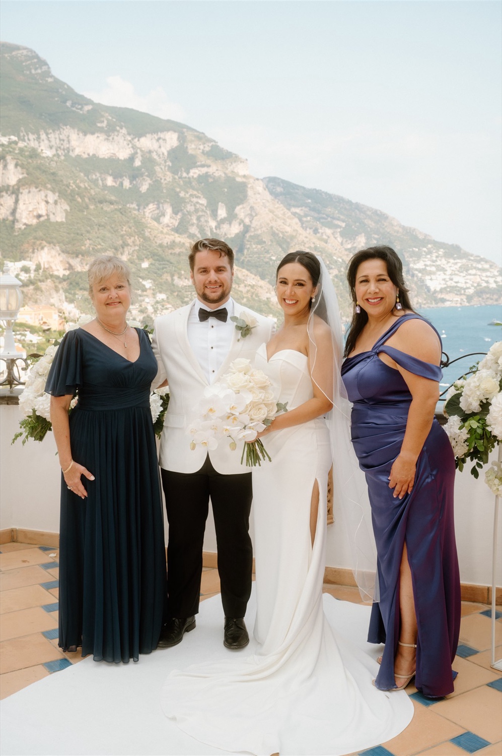 A bride and groom with their guests on the rooftop terrace of Hotel Conca d’Oro in Positano, with the mountains of Positano behind