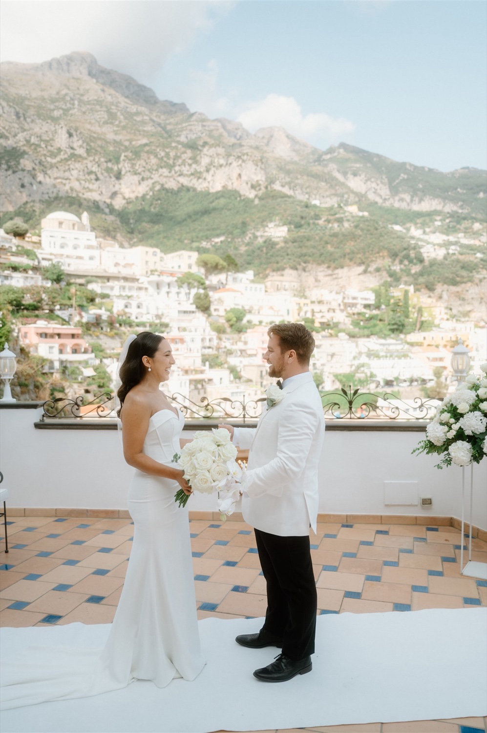A couple exchanging vows on the rooftop terrace of Hotel Conca d’Oro in Positano, with the village behind them