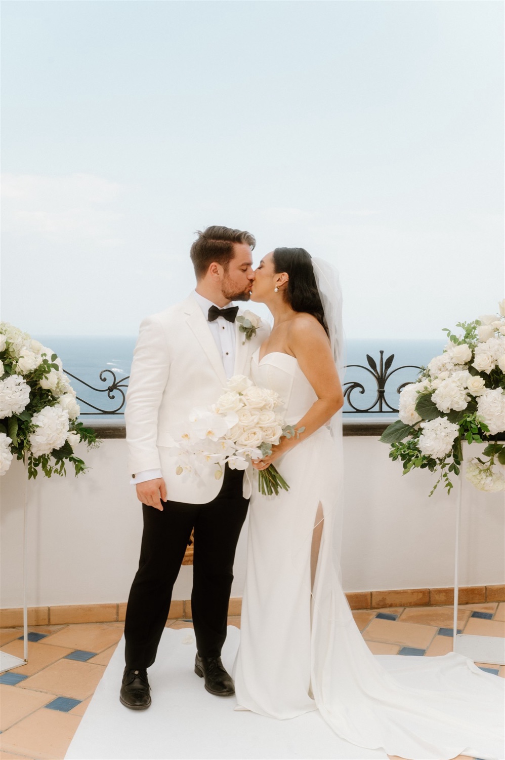 A couple kissing between white flower arrangements on the rooftop terrace of Hotel Conca d’Oro in Positano