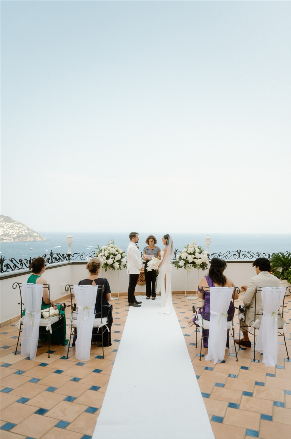 A small ceremony with guests seated on the rooftop terrace of Hotel Conca d’Oro in Positano, with the sea behind