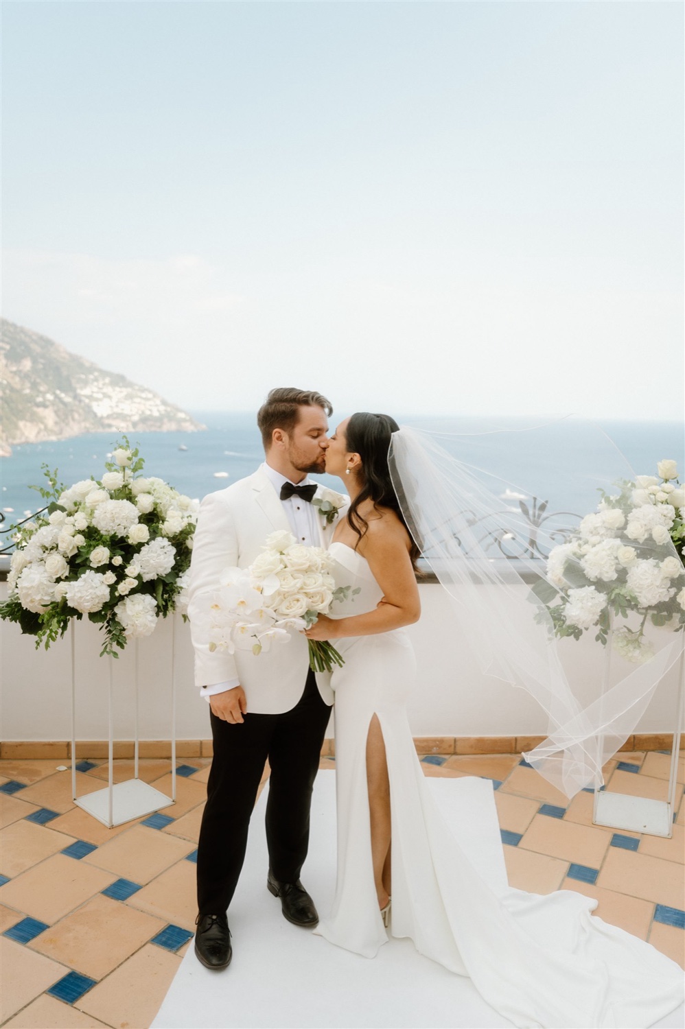 A couple kissing on the rooftop terrace of Hotel Conca d’Oro in Positano, with white flowers beside them