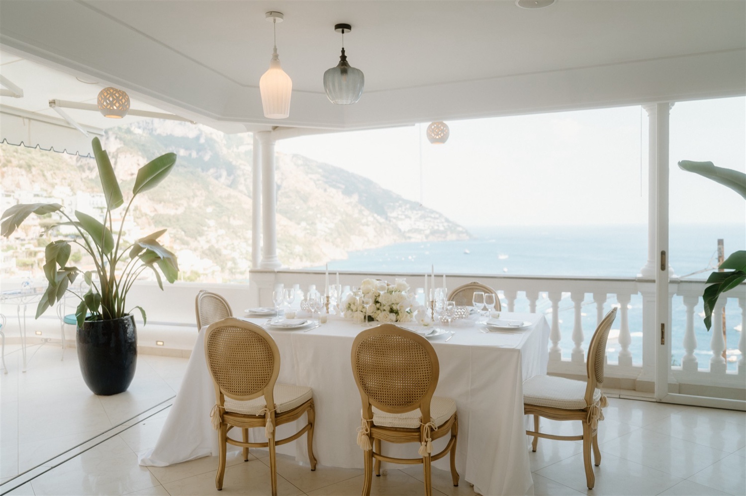 The covered dining terrace of Hotel Conca d’Oro in Positano, with a table set for two and views of the coast