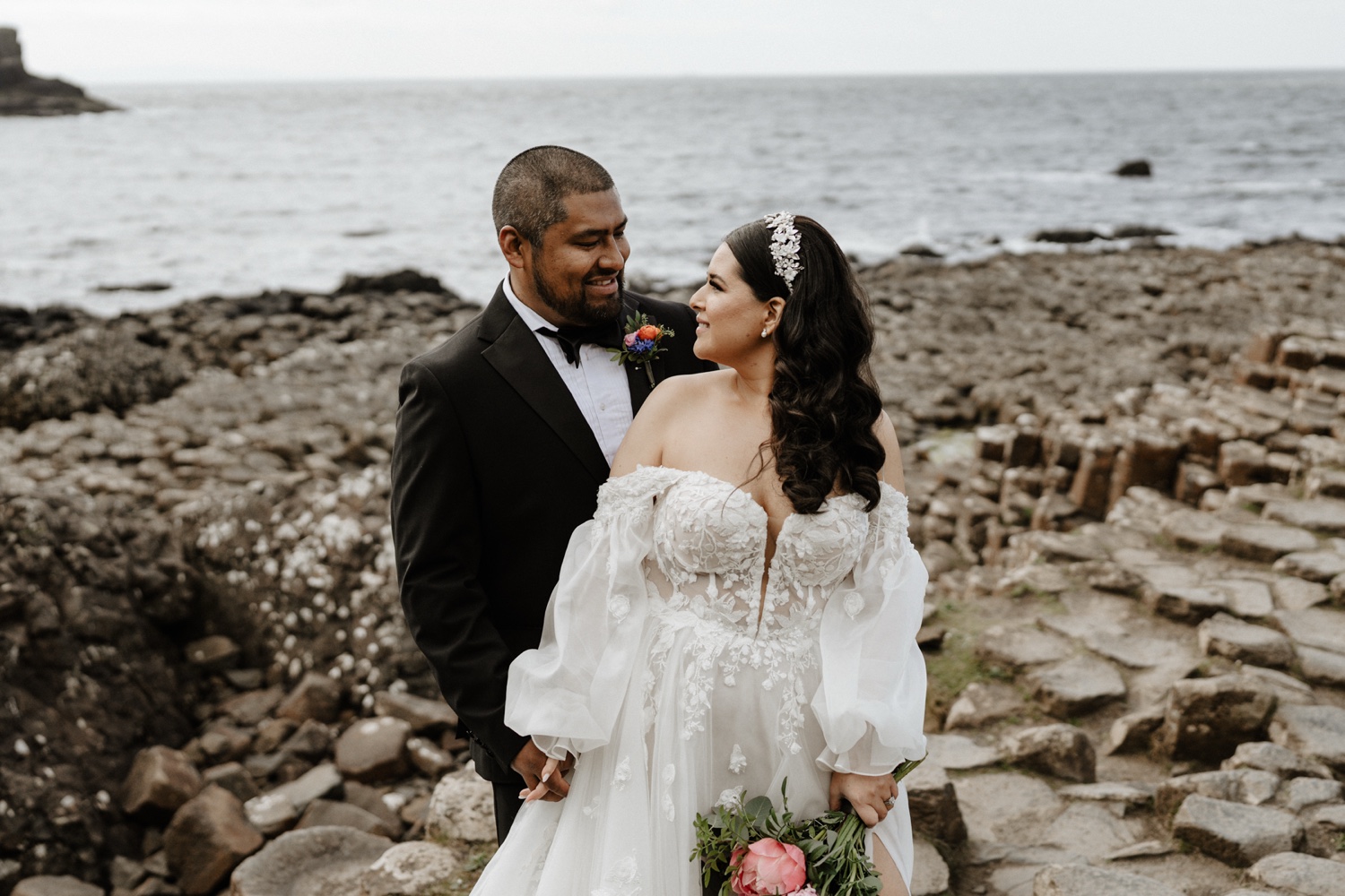 A groom and bride smiling at each other on the rocks of the Giant's Causeway in Northern Ireland