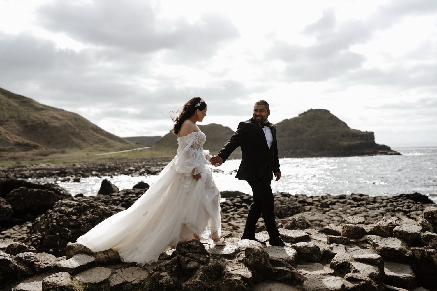A bride and groom holding hands as they walk across the basalt rocks of the Giant's Causeway in Northern Ireland