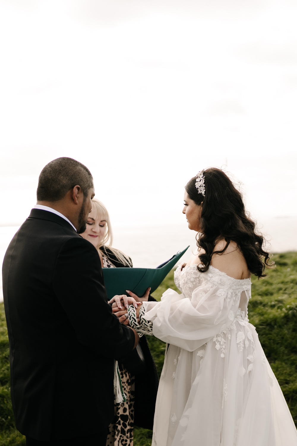 A groom and bride exchanging rings with their celebrant on the clifftops near Dunluce Castle, Northern Ireland