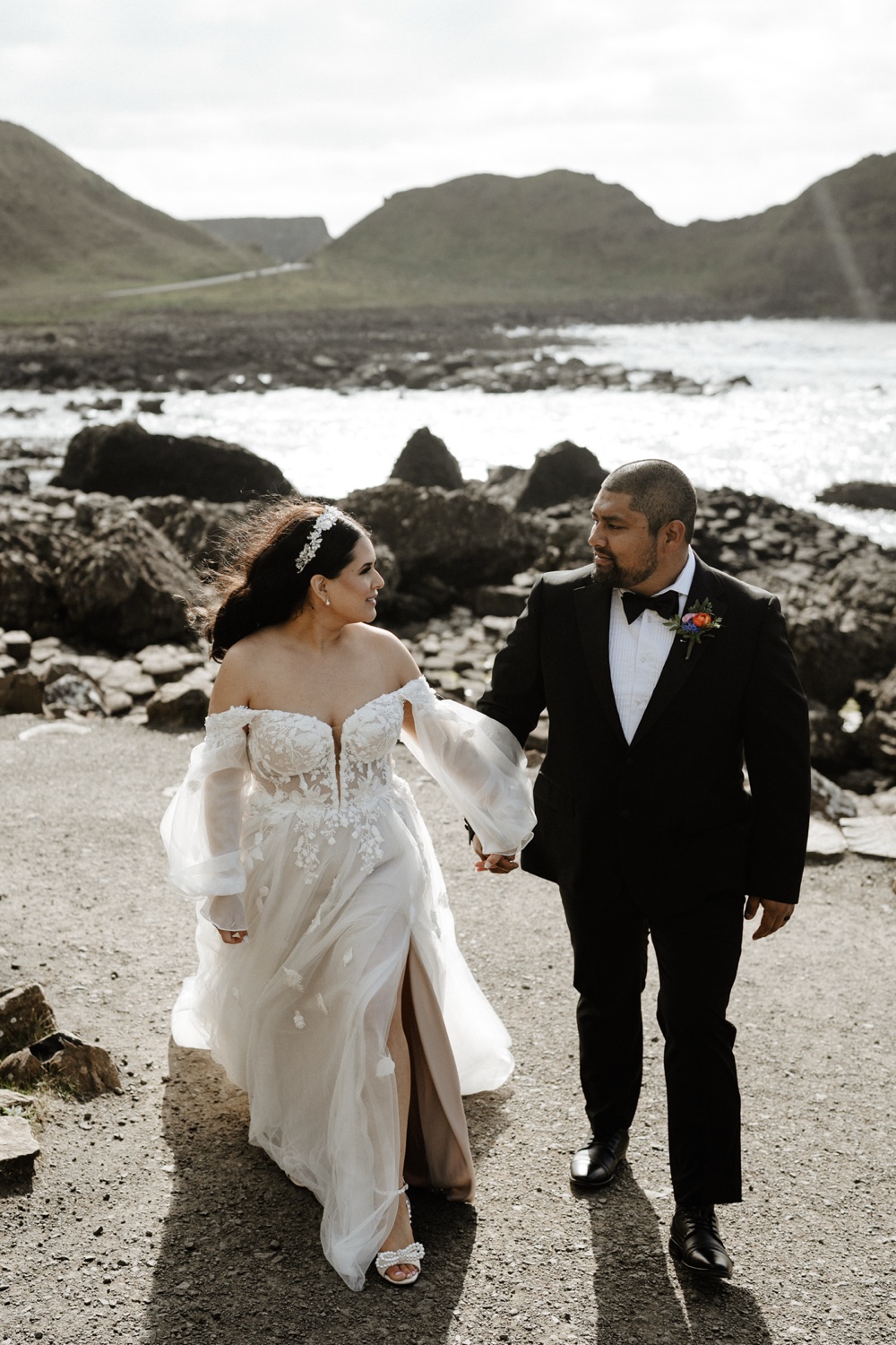 A bride and groom walking hand in hand along a coastal path near the Giant's Causeway in Northern Ireland