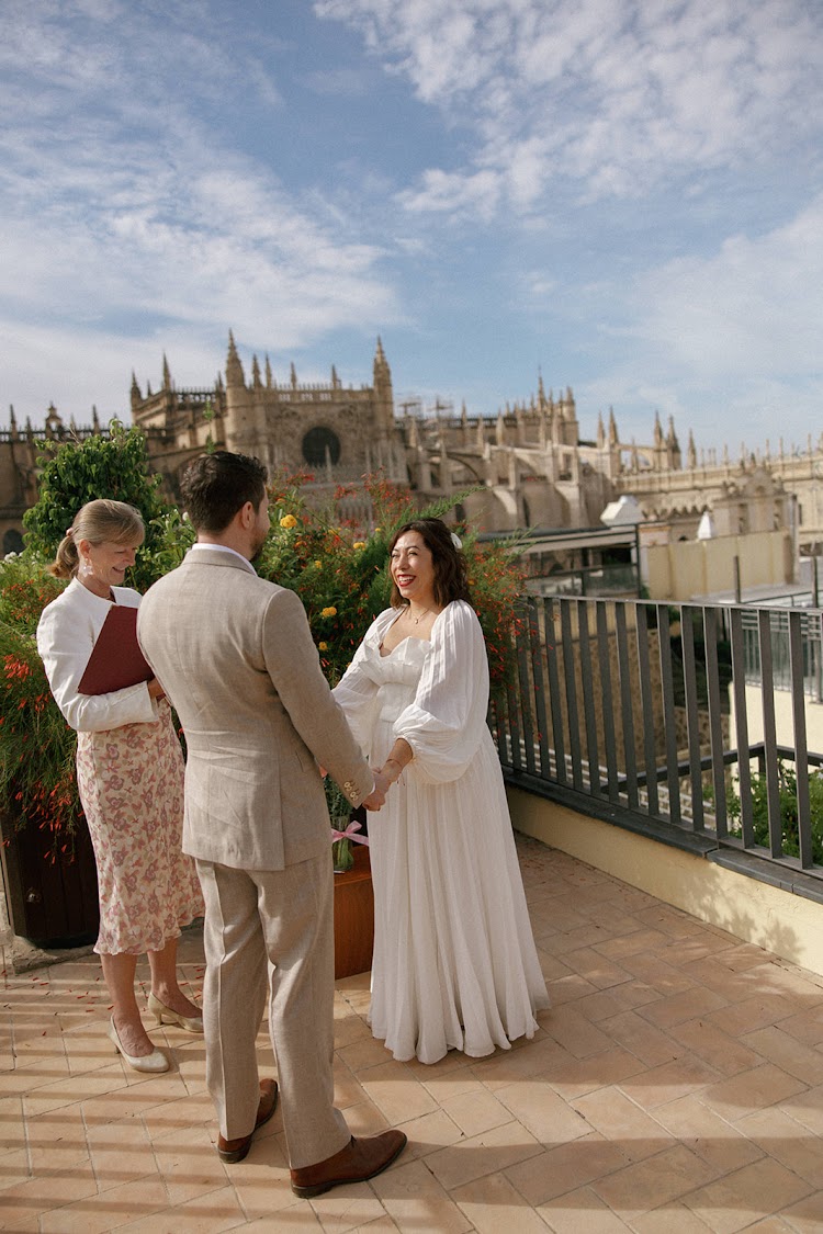 A couple holding hands during their elopement ceremony on the terrace of EME Catedral Mercer in Seville, with Seville Cathedral behind