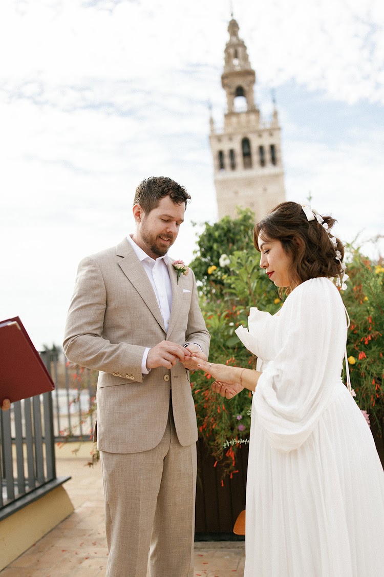 A couple exchanging rings on the rooftop terrace of EME Catedral Mercer in Seville, with the Giralda tower behind