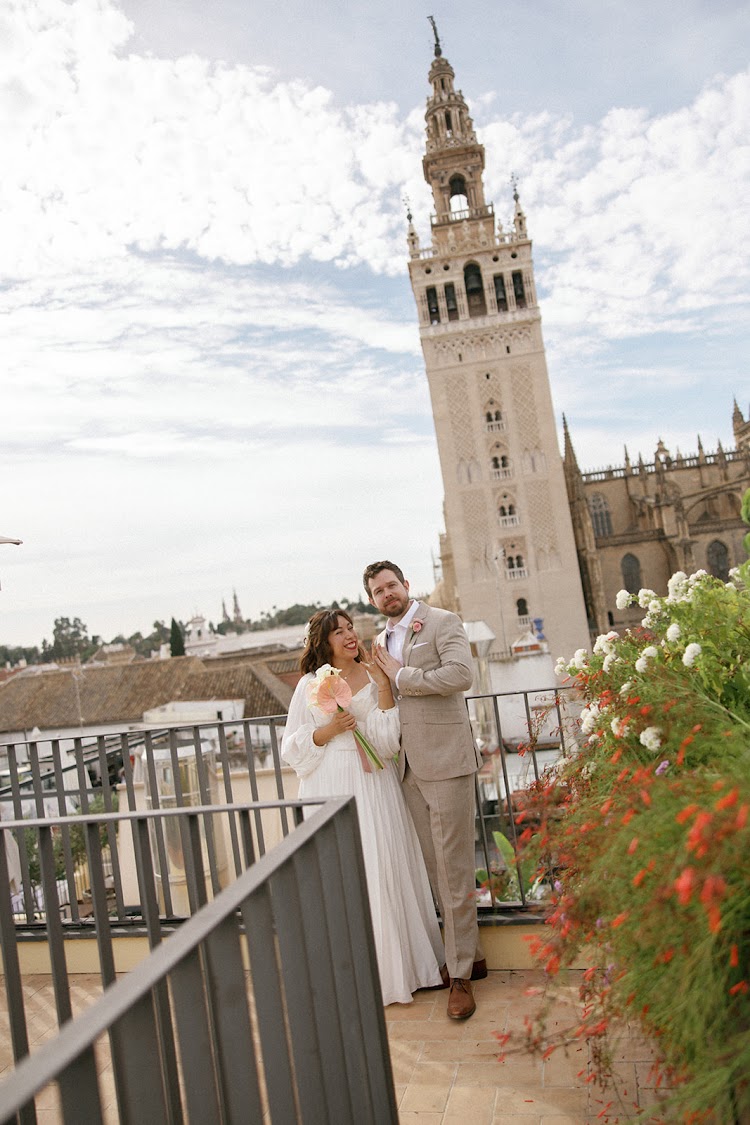 A bride and groom close together on a terrace at EME Catedral Mercer in Seville, with the Giralda tower behind them