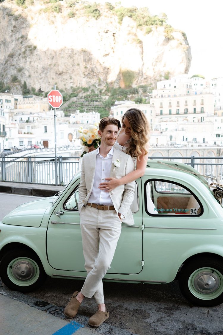 A groom beside the vintage car, above the sea