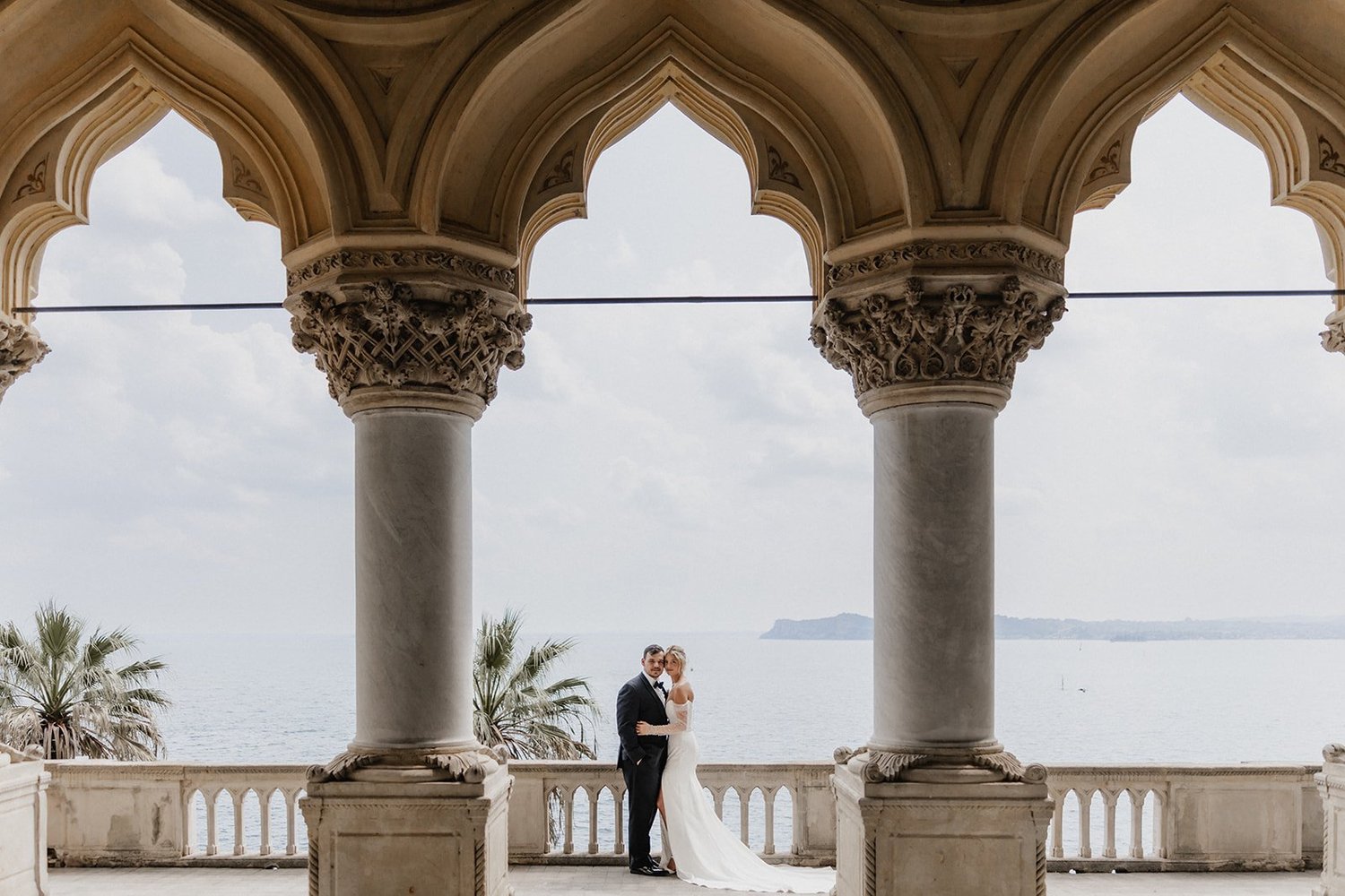 A couple under the Gothic loggia of the villa on Isola del Garda, looking out over the lake