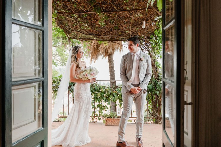 A bride and groom standing under a vine-covered pergola during their elopement in Sicily