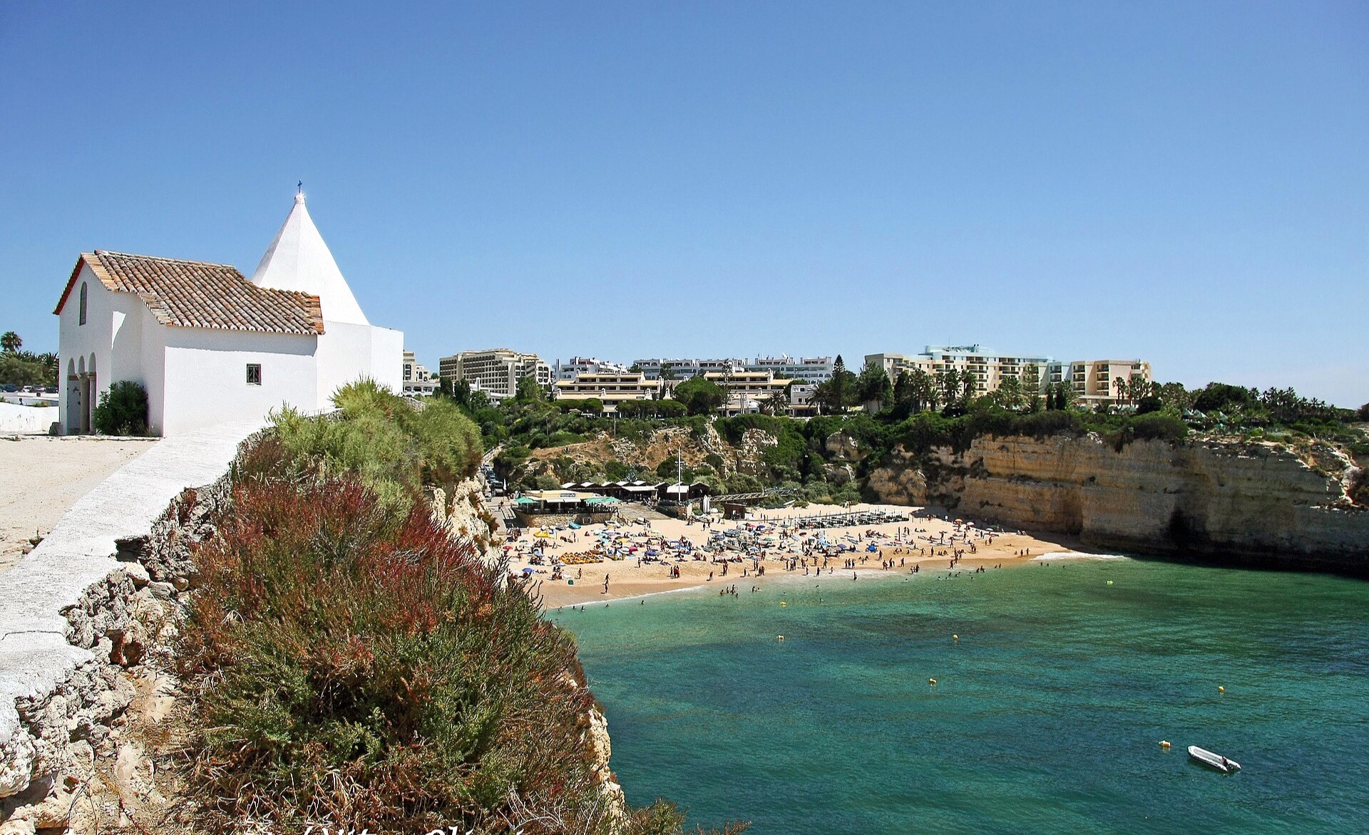 The chapel of Lady of the Rock seen from the cliff above the beach, with the coast of the Algarve beyond