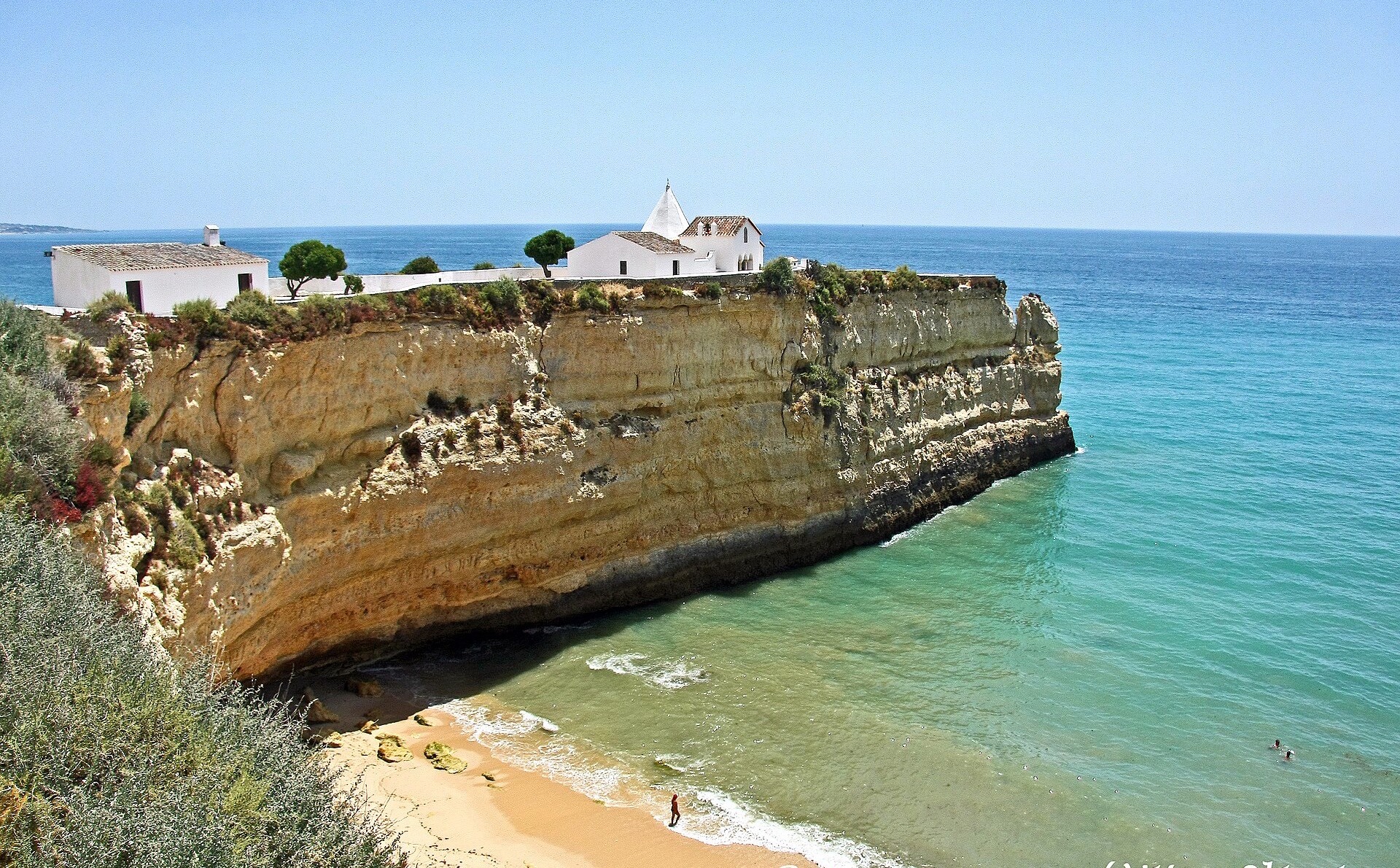 The chapel of Lady of the Rock on its orange cliff above the green sea on the Algarve coast, Portugal