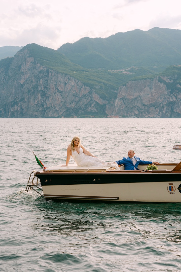 A couple in a classic wooden boat on Lake Garda with the mountains behind them
