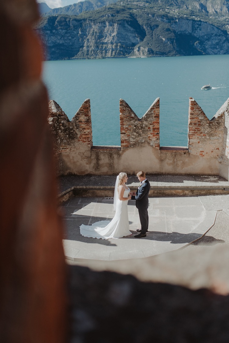 A couple sitting close together in front of the castle rock of Malcesine, Italy