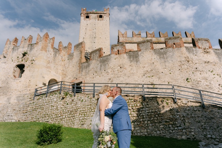 A bride and groom kissing in front of the stone walls of the Scaliger Castle in Malcesine