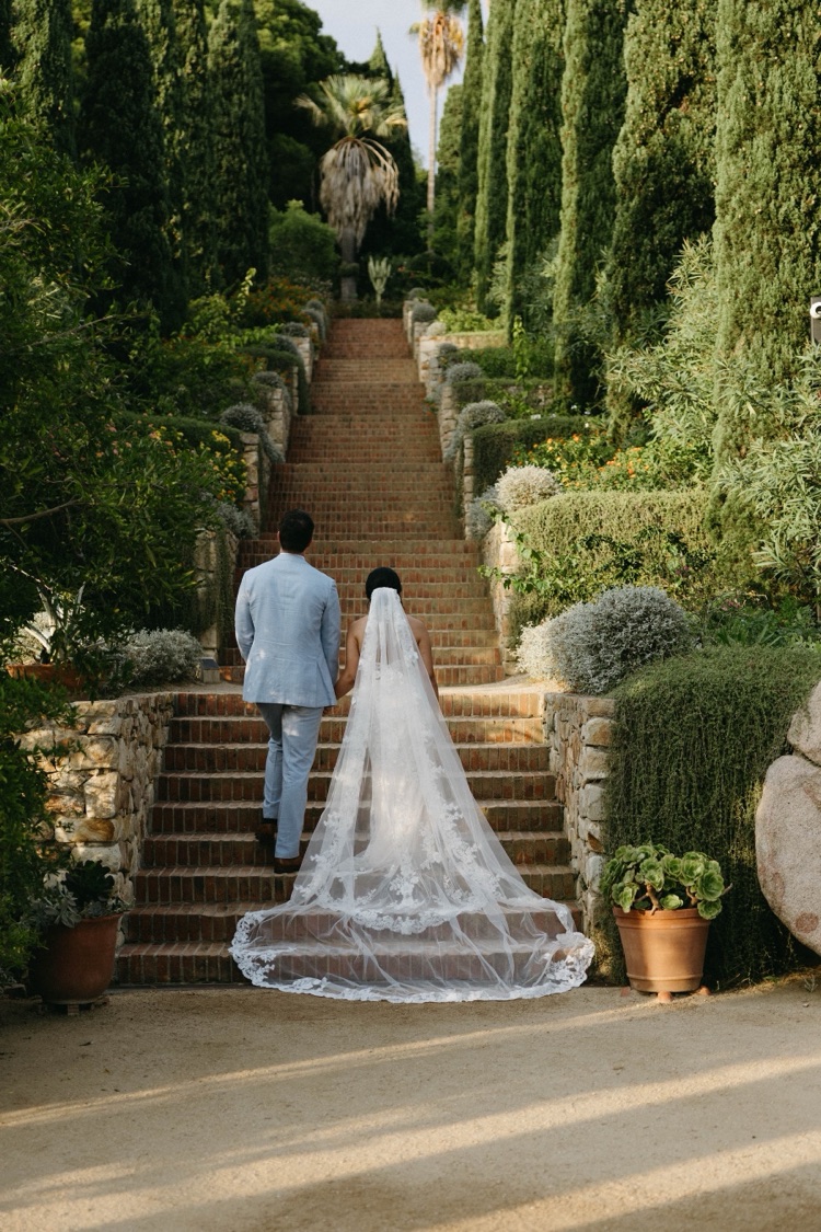 A bride and groom climbing the brick stairway lined with cypress trees at Marimurtra Botanic Gardens, Blanes