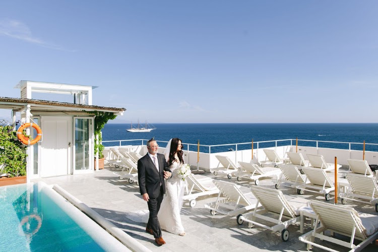 Bride and her escort walking towards the ceremony past the pool at the rooftop of Hotel Marina Riviera on the Amalfi Coast, Amalfi Coast