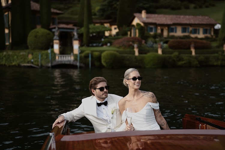 A couple on a wooden boat, with a lakeside villa behind