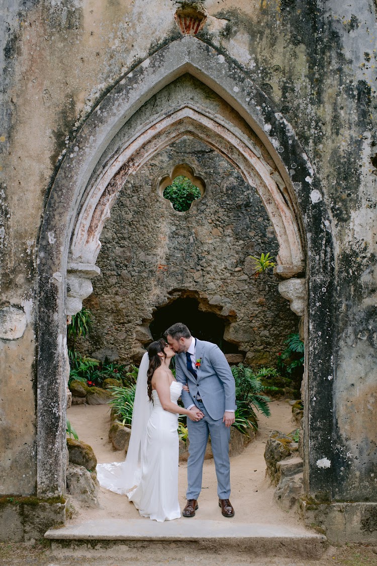A couple kissing beneath the Gothic stone arch of the Ruin Chapel at Monserrate Palace in Sintra, Portugal